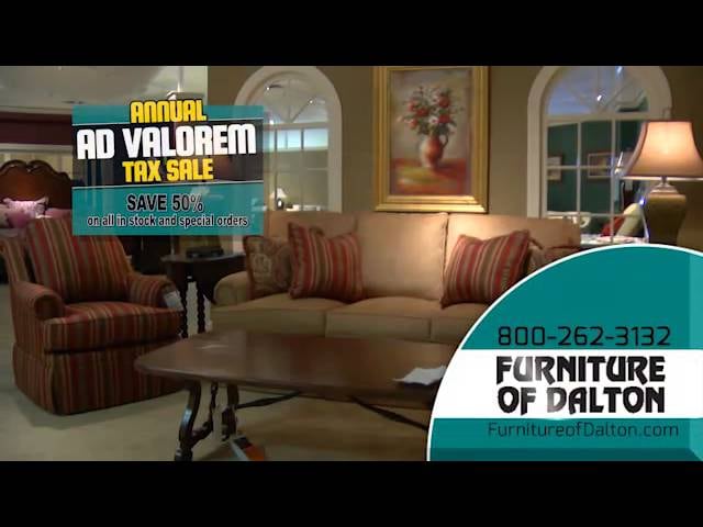 Frame from a commercial: a furnished living room with an annual tax-sale banner and the store's phone number